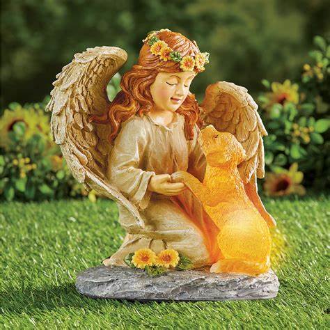 Garden statue of an angel girl with wings and flower crown kneeling beside a glowing golden dog on grass