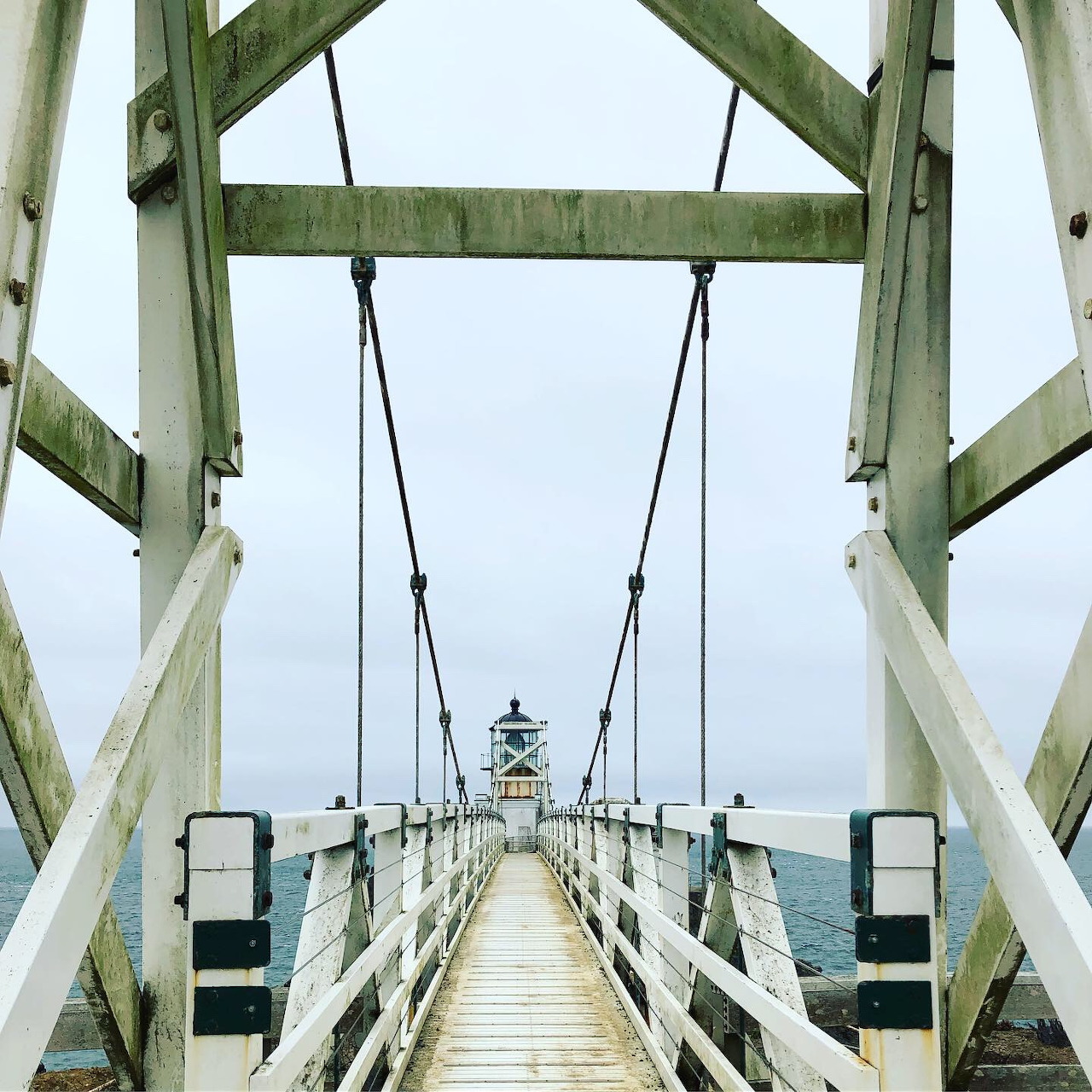 Wooden walkway leading to Point Reyes Lighthouse beneath overhead beams and a pale sky