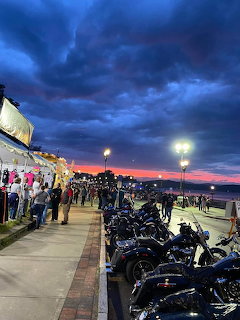 Parked motorcycles along a boardwalk with crowds and dramatic sunset sky