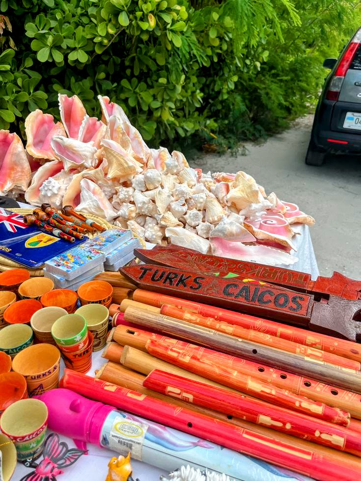 Outdoor souvenir stall with seashells, colorful wooden flutes, ceramic mugs, and a Turks and Caicos sign.