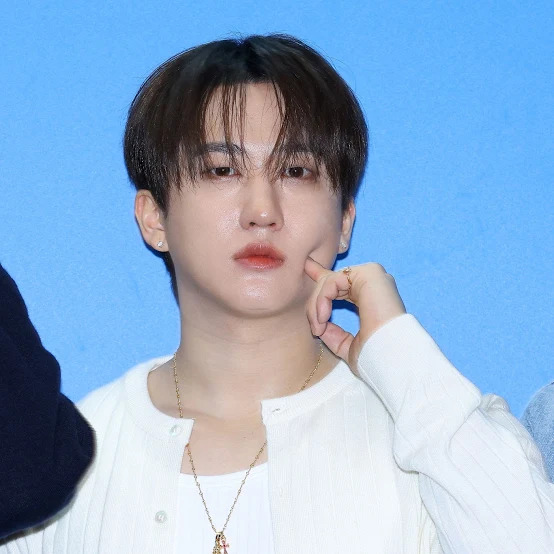 Young man in white shirt with jewelry posing against blue backdrop