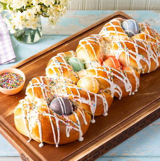 Braided Easter bread with colorful eggs and white icing drizzle on wooden board