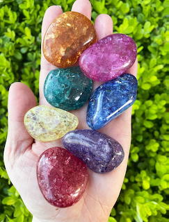 Hand holding seven colorful polished gemstones arranged vertically against green leaves