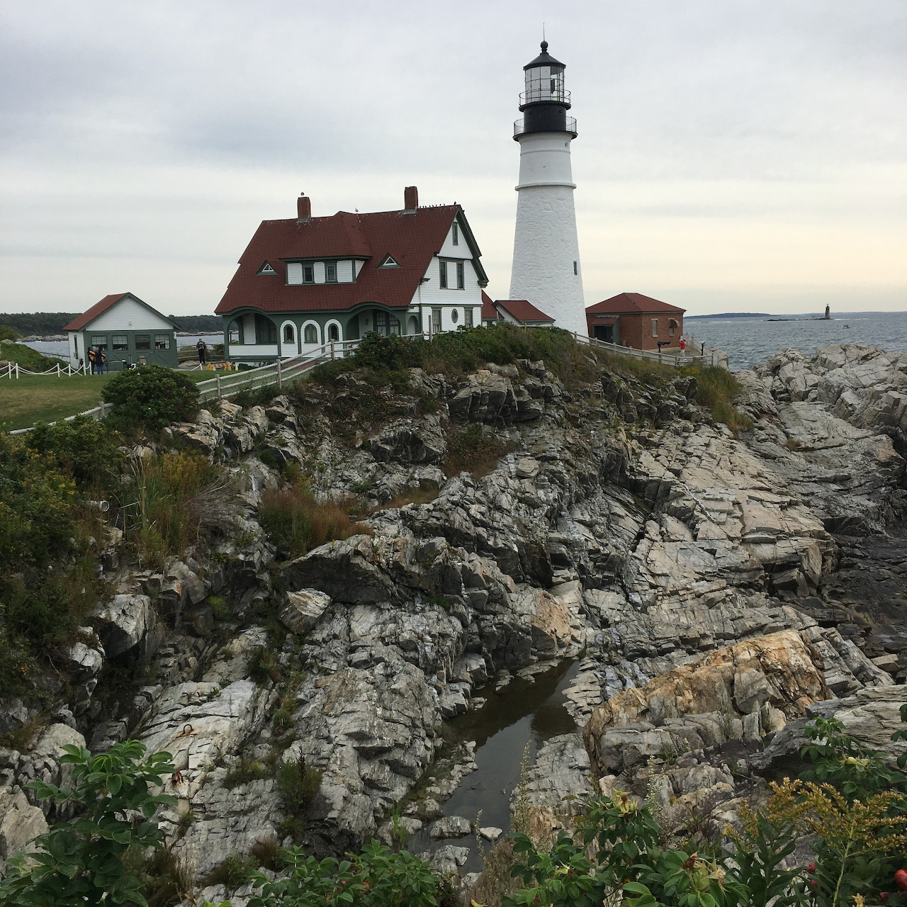 White lighthouse and red-roofed house on rocky coastal cliff with ocean view