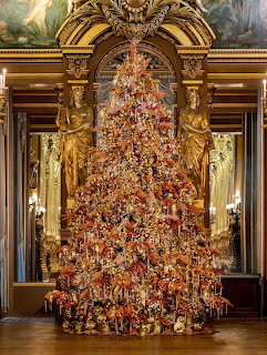 Lavishly decorated Christmas tree with colorful ornaments in ornate Victorian room with golden arch