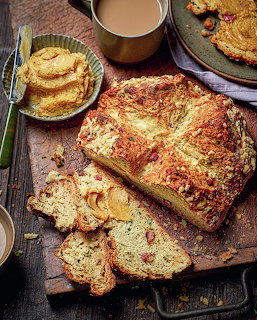 Sliced banana bread loaf on wooden cutting board with butter, cookies, and coffee mug