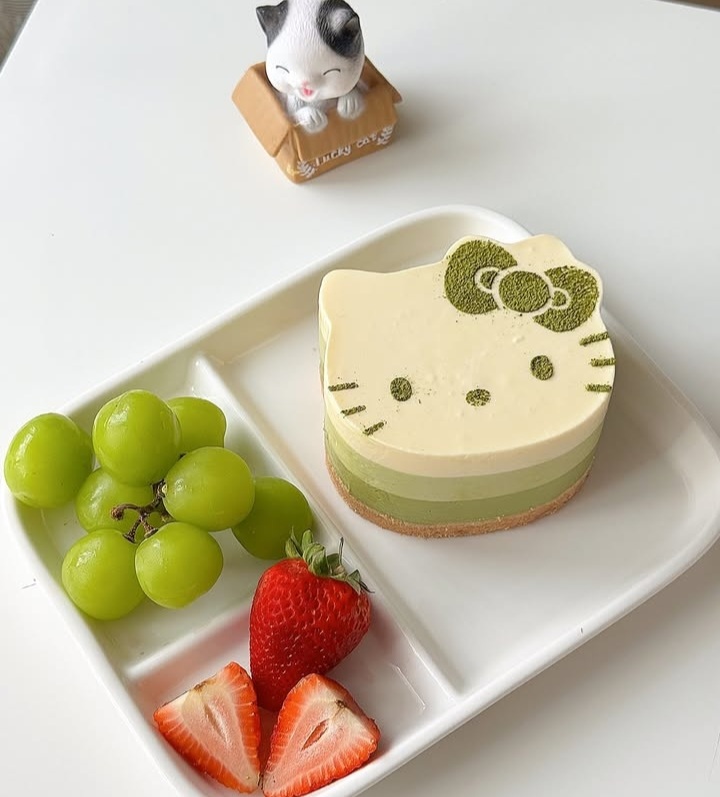 Hello Kitty-shaped green and cream layered pastry with strawberries and grapes on white plate