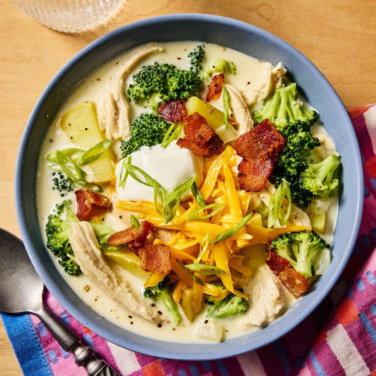 Bowl of creamy chicken soup with broccoli, bacon, cheese, and sour cream on a wooden table