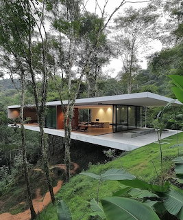 Modern glass house with flat white roof surrounded by dense tropical jungle on a green hillside