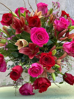 Bouquet of vibrant pink and red roses with orange lilies and green foliage