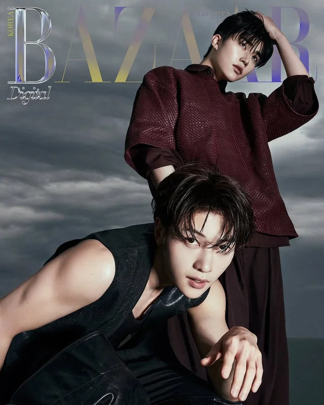 Two young men in dark fashion styling pose for magazine cover with cloudy sky background