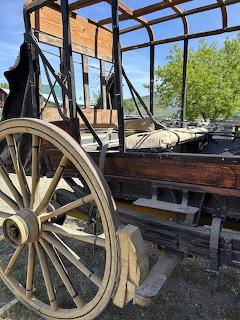 Antique wooden stagecoach with large yellow spoked wheel being restored outdoors