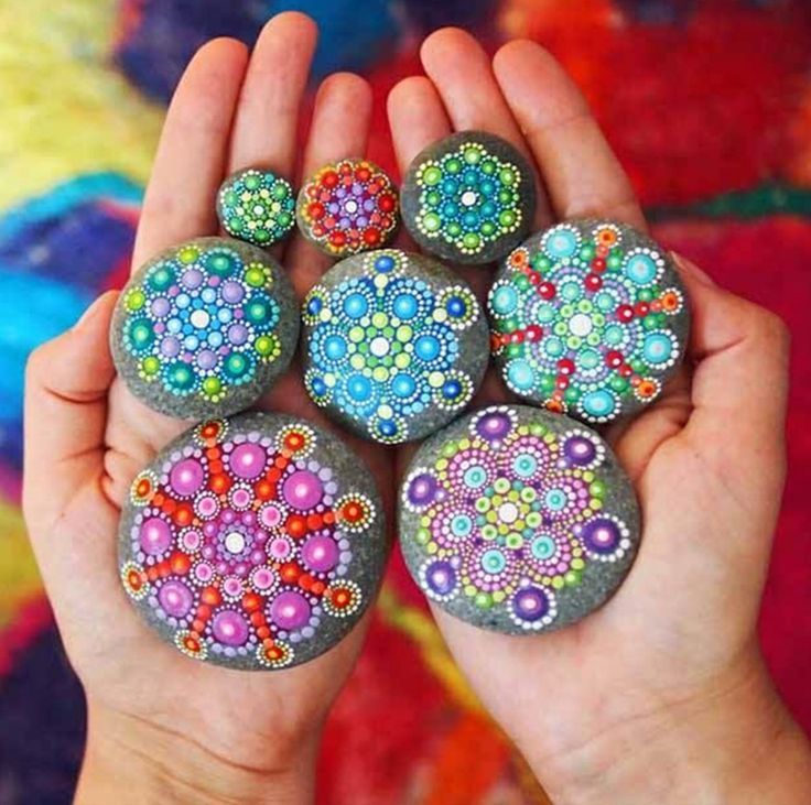 Two hands holding six colorful stones painted with mandala dot patterns