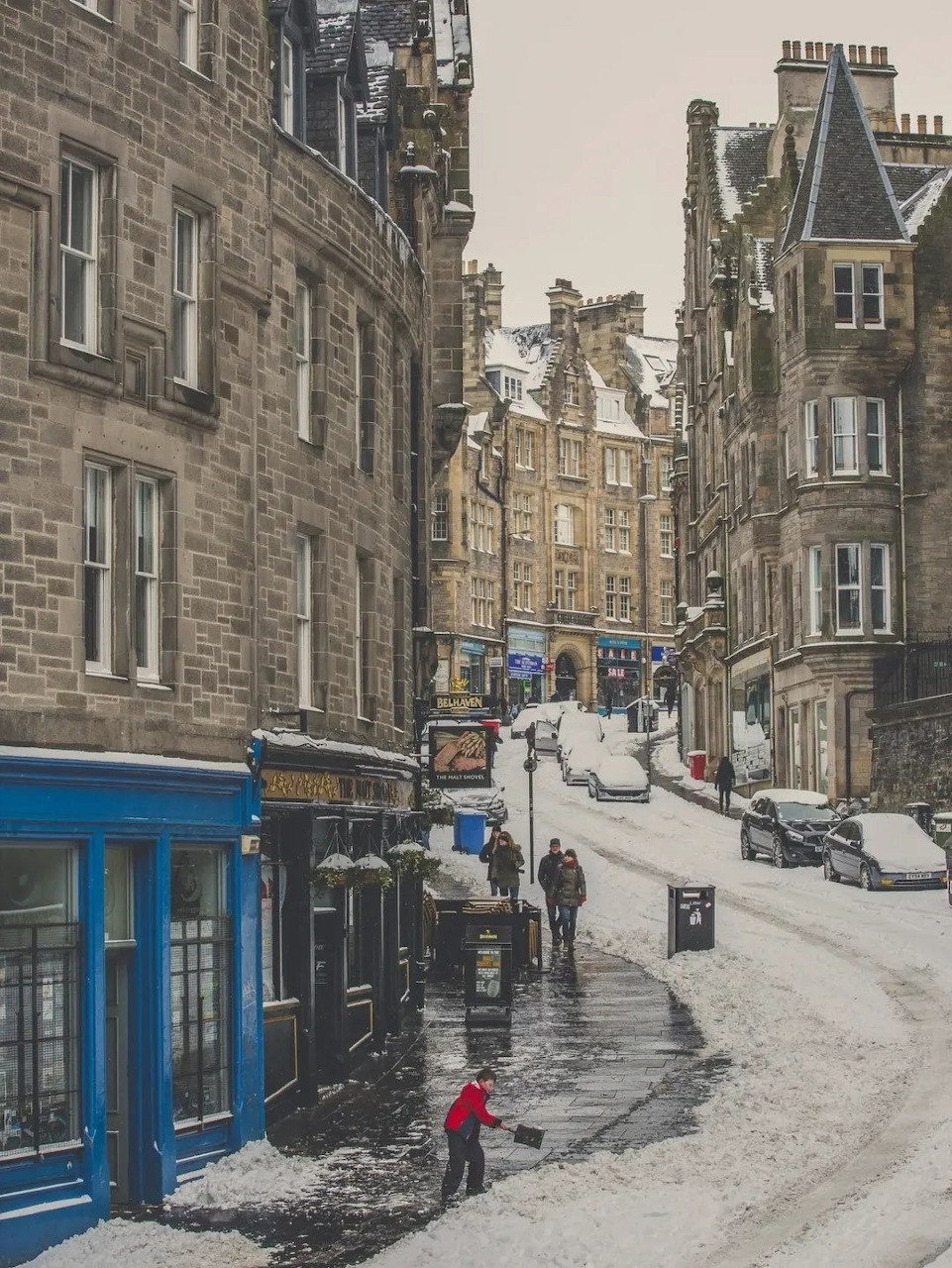 Snow-covered Edinburgh Old Town street with historic stone buildings and pedestrians in winter