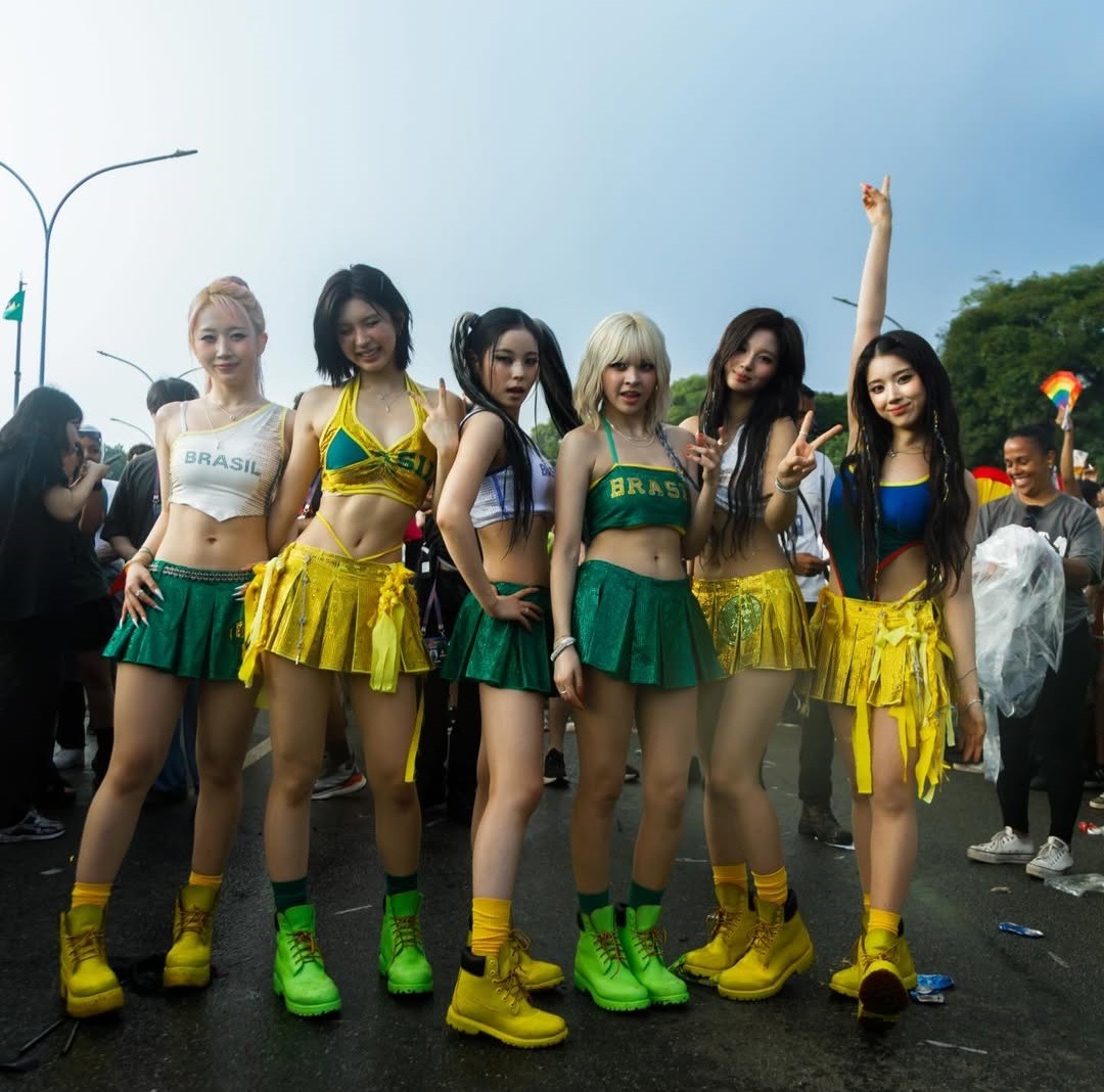 Seven women in bright yellow, green, and blue performance outfits posing together outdoors