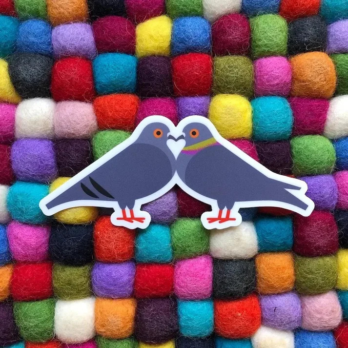 Sticker of two cartoon pigeons touching beaks on a colorful felt ball background