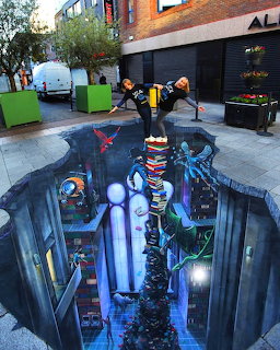 3D street art showing an illusionary vertical underground city tower painted on pavement with people viewing