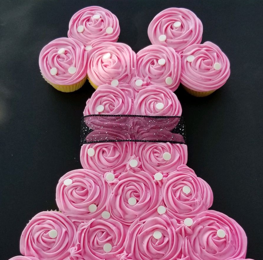 Pink frosted cupcakes arranged like a dress on a dark background