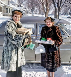 Two women in fur coats holding Christmas gifts beside a car on a snowy street