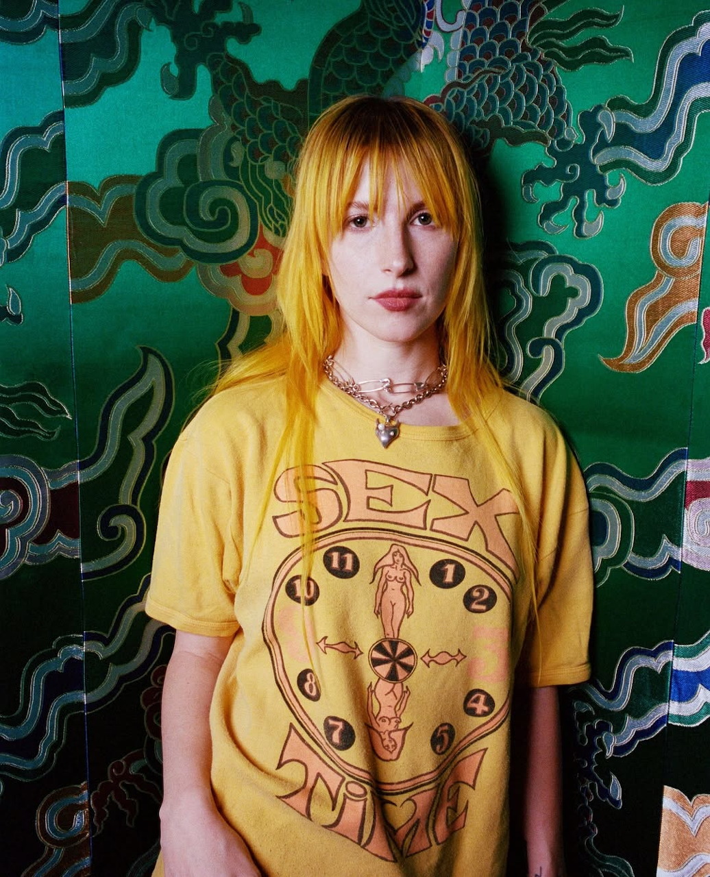Young woman with yellow hair and yellow graphic t-shirt against a green dragon wallpaper background
