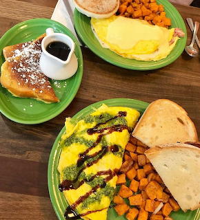 Three green plates with omelettes, french toast, sweet potatoes and bread on a wooden table