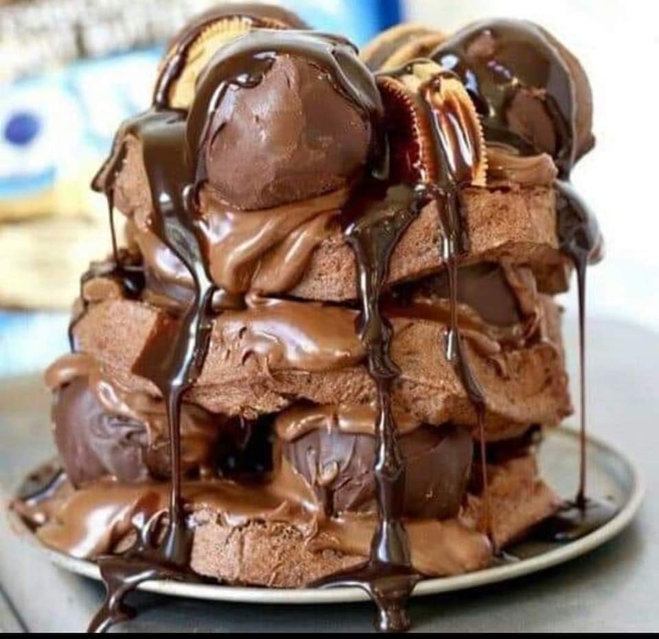 Tall chocolate layer cake decorated with truffles, chocolate curls, dripping sauce, and pecans