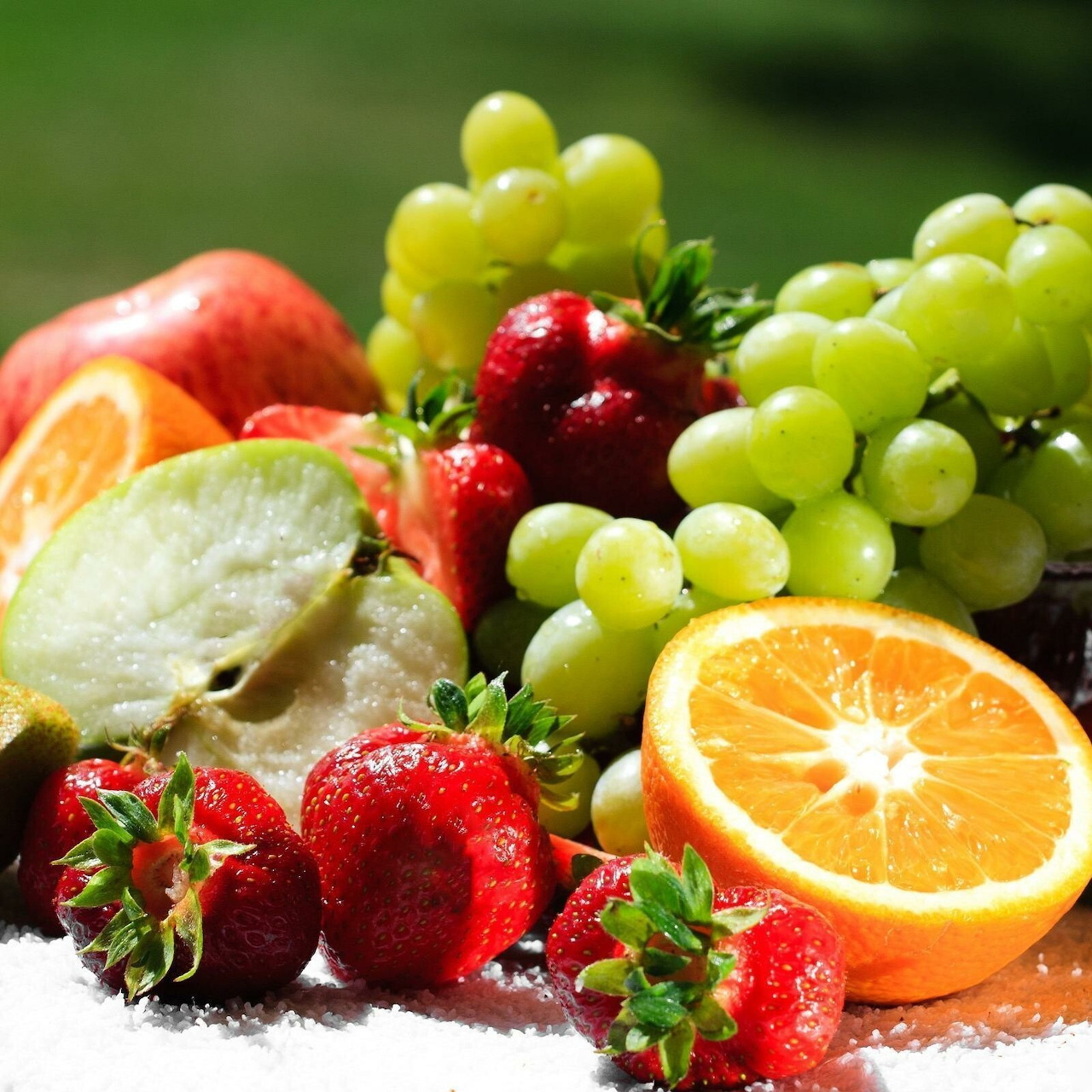 Assorted fresh fruits with grapes, strawberries, orange slices and apple arranged on white surface