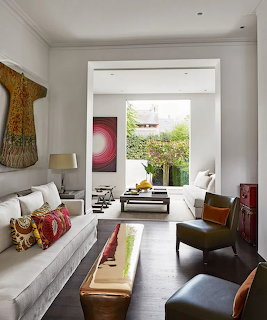 Modern white living room with sofas, colorful pillows, artwork, and garden view through open doorway
