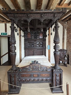 Ornately carved dark walnut four-poster bed with canopy in a historic room with wooden beams