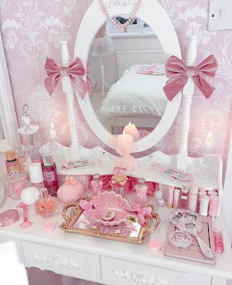 Pink vanity table with oval mirror, pink bows, candles, perfume bottles, and decorative accessories