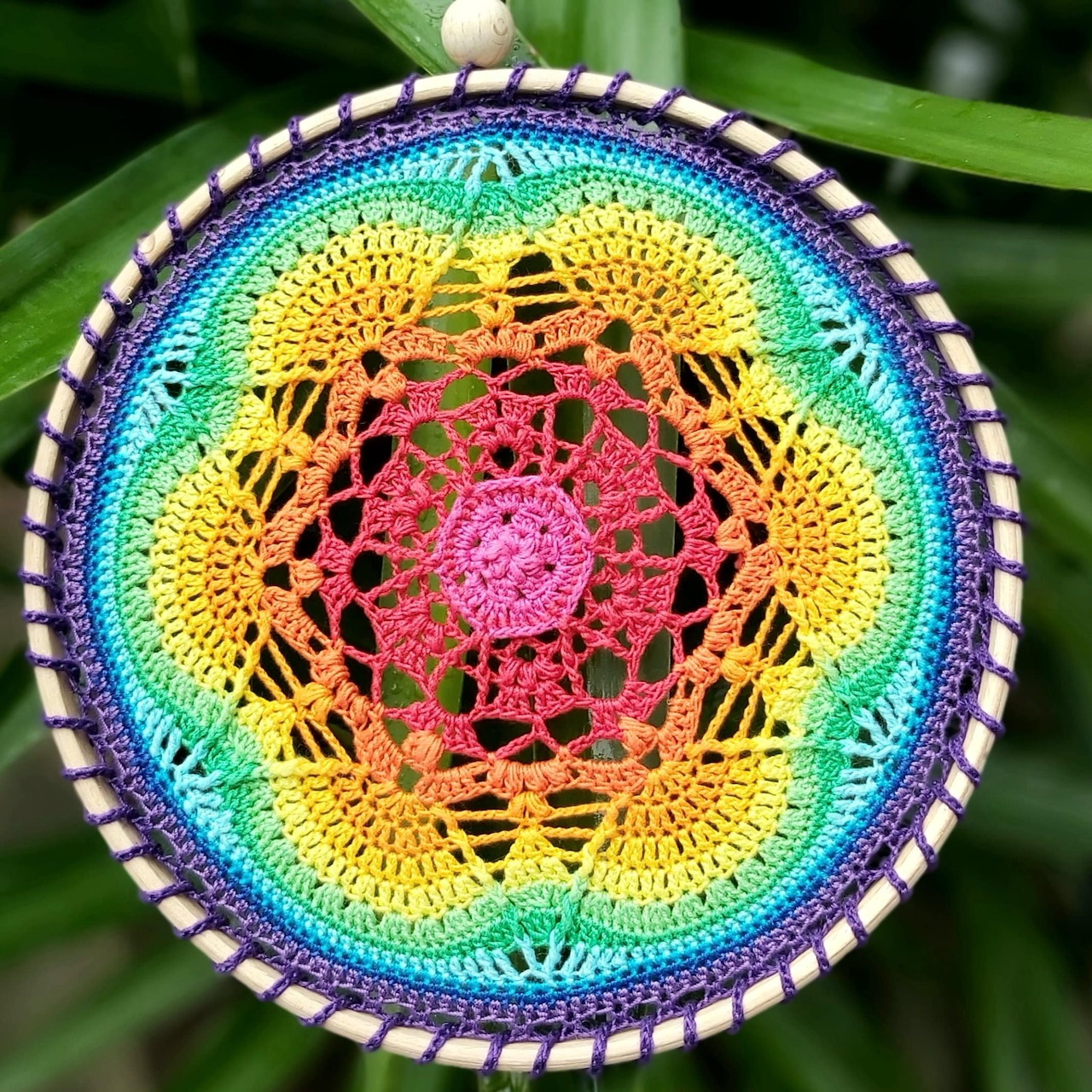 Handmade circular crochet mandala in rainbow colors with intricate lace pattern and white scalloped border