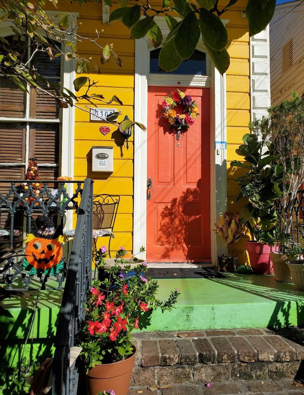 Yellow house with orange door and Halloween decorations on small porch with green floor and potted plants