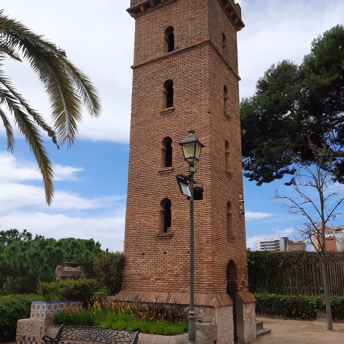 Tall red brick tower with palm trees and blue sky in Barcelona