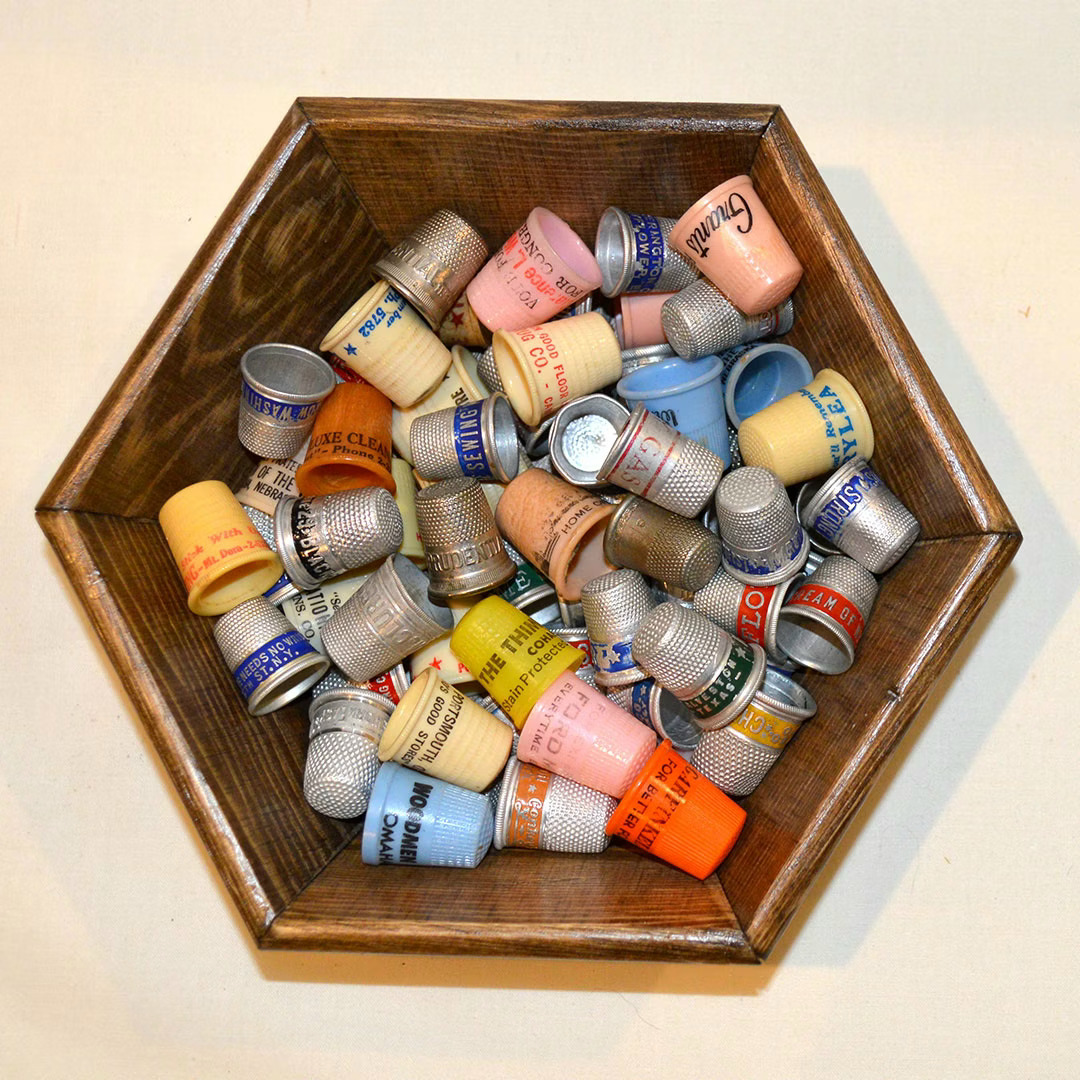 Collection of colorful vintage advertising thimbles arranged in a hexagonal wooden display tray