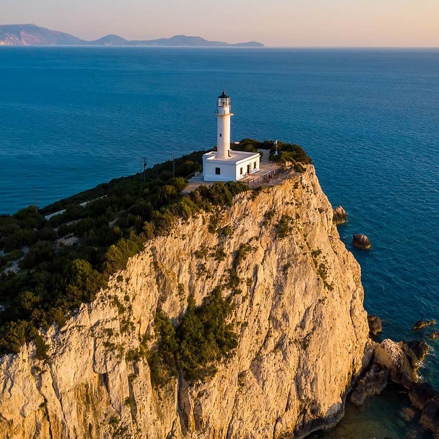 White lighthouse perched on steep cliff edge above blue sea at golden hour