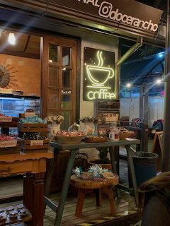 Cozy cafe entrance with a neon coffee sign, wooden decor, and tables of baked goods
