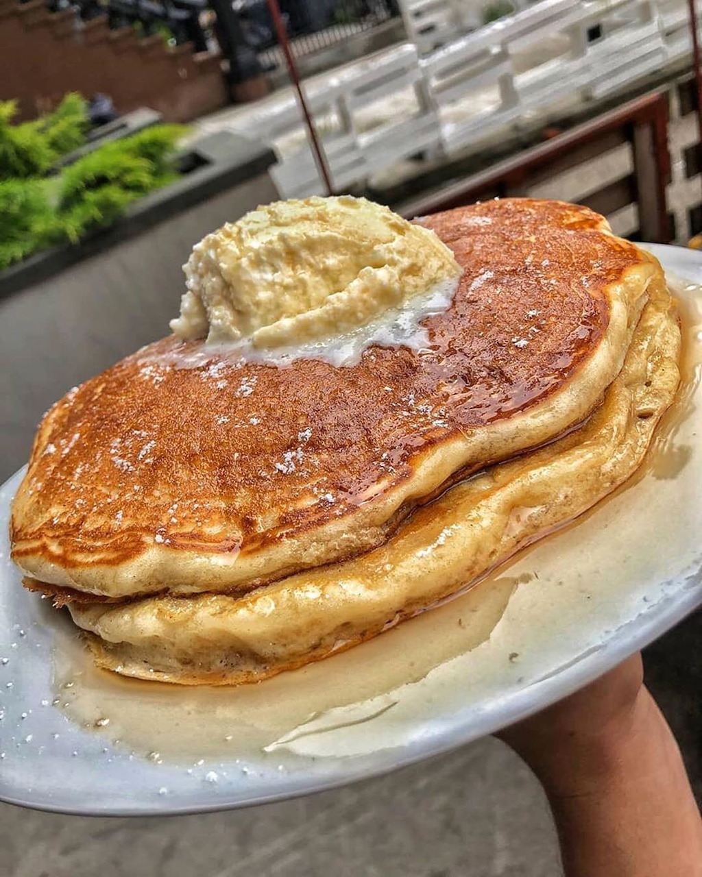 Close-up of golden pancakes on a plate with a scoop of butter and powdered sugar