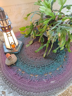 Leafy potted plant on a round crocheted rug beside a decorative lantern and small stone