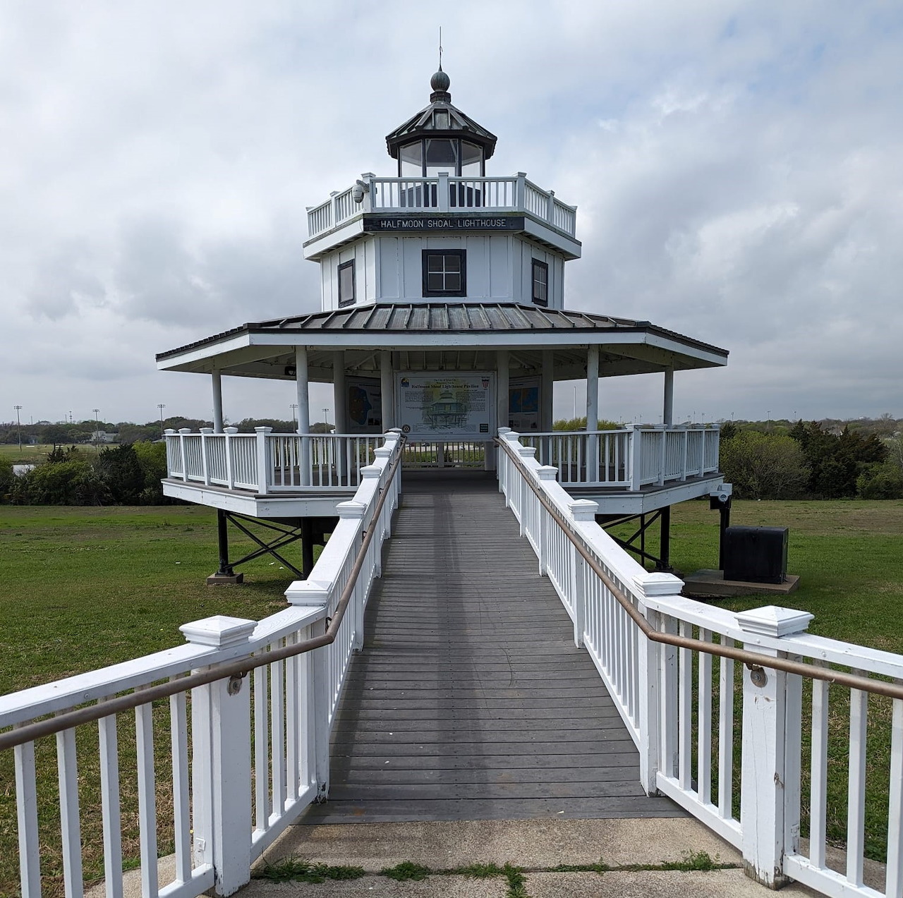White lighthouse with black dome on elevated boardwalk over grassy coastal area
