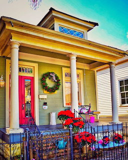 Yellow house with Christmas wreath, red door, poinsettias and holiday decorations on porch