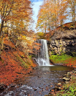 Waterfall cascading over rocky cliffs surrounded by colorful autumn trees in orange and red