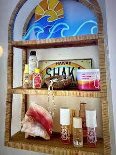 Wicker shelf with tropical decor including conch shell, sunscreen, Hawaii plate, and painted sun and waves