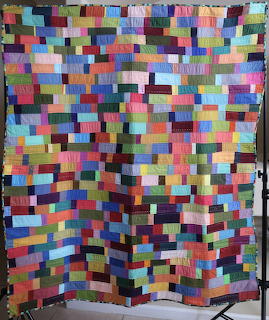 Colorful patchwork quilt hanging with small rectangular fabric patches in various colors arranged in rows