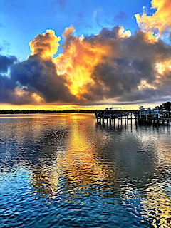 Colorful sunrise over calm water with golden reflections and a wooden dock under dramatic clouds