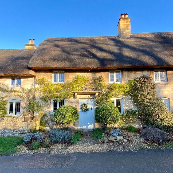 Traditional stone cottage with thick thatched roof, light blue door, climbing plants, and gravel garden path
