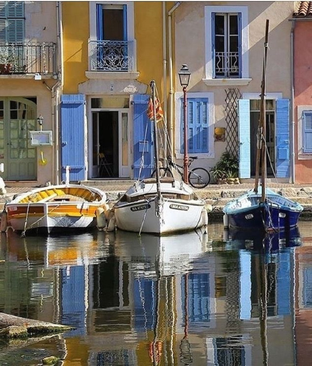 Colorful houses with blue shutters reflected in a canal with mored boats