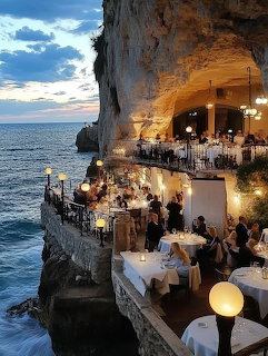 Cliffside restaurant terraces lit at dusk above the ocean beside a rocky coastal cliff