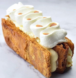 Close-up of a mille-feuille pastry with flaky crust, cream filling, and whipped cream topping