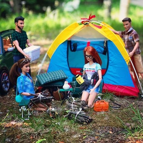 Barbie and Ken dolls camping with a colorful tent, campfire, and outdoor accessories in a green forest