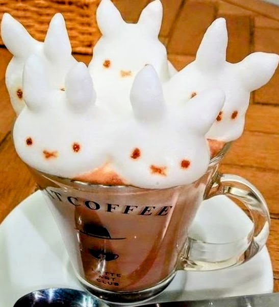 Coffee mug with 3D foam art shaped like three white bunnies with dots for features